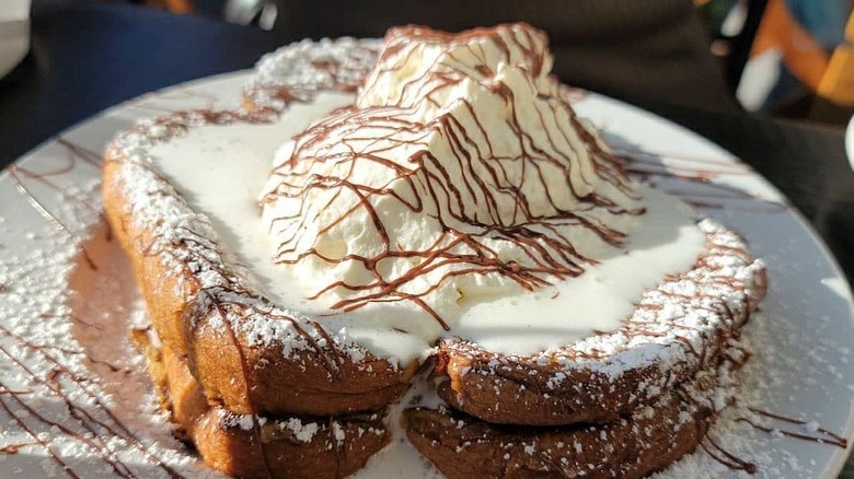 french toast on a plate covered in whipped cream, powdered sugar, and chocolate sauce