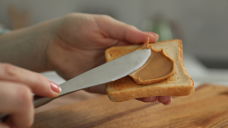 A knife spreads peanut butter onto toast.