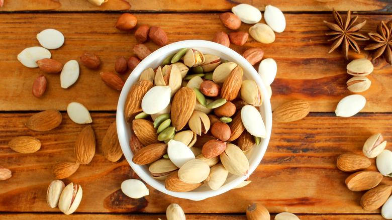 A variety of nuts sit in a bowl on a wooden table.