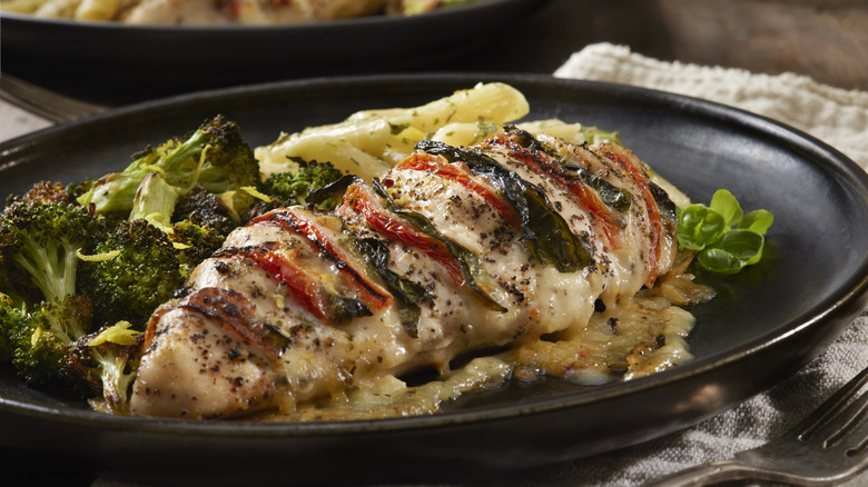 Caprese chicken breast next to broccoli and other vegetables.