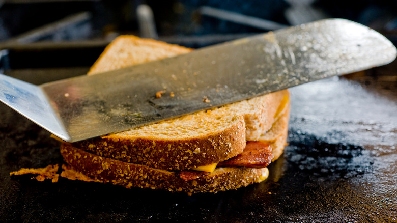 Using a spatula to press down on a grilled and bacon cheese sandwich.