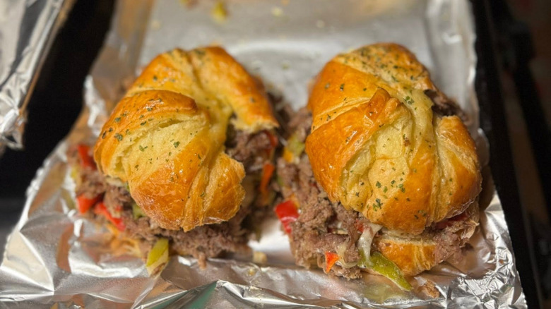 Croissant cheesesteaks sit on a foil-lined pan.
