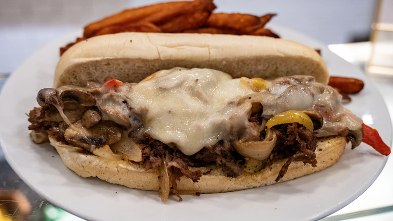 A cheesesteak sits on a white plate.