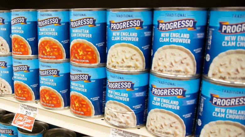 Can of clam chowder are on a grocery store shelf.