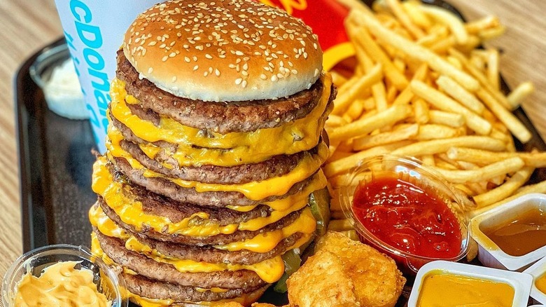 A McDonald's secret menu Monster Mac next tofries, nuggets. sauce pots, and a drink.