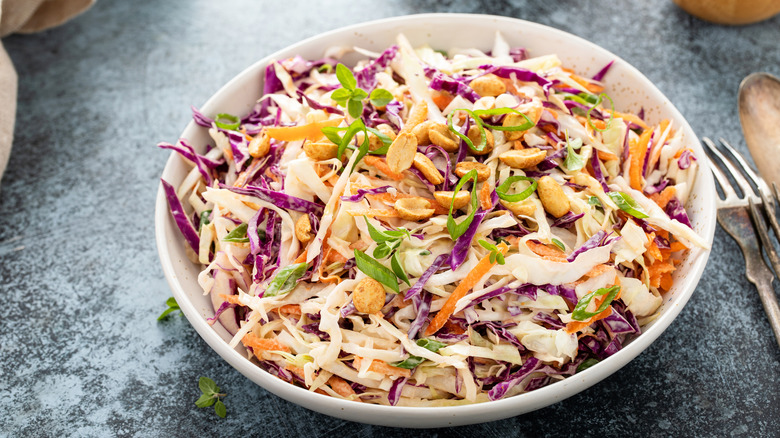 A bowl of coleslaw, topped with thinly sliced green onion and peanuts.