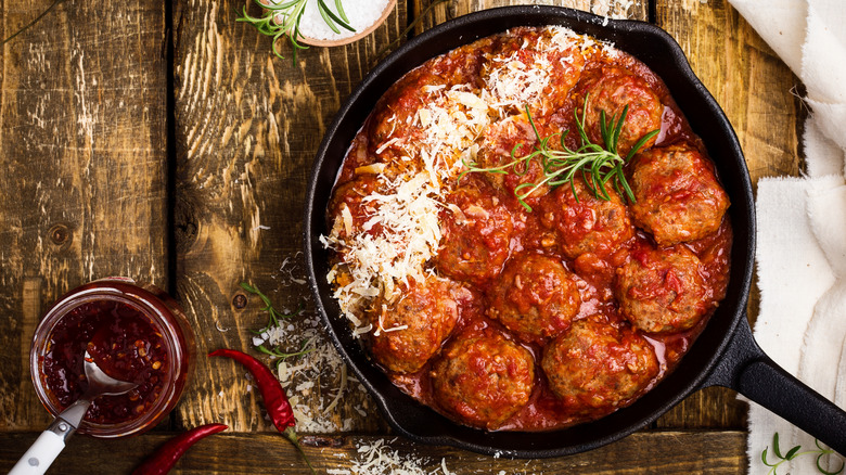 Meatballs in red sauce with grated cheese on top on wooden table