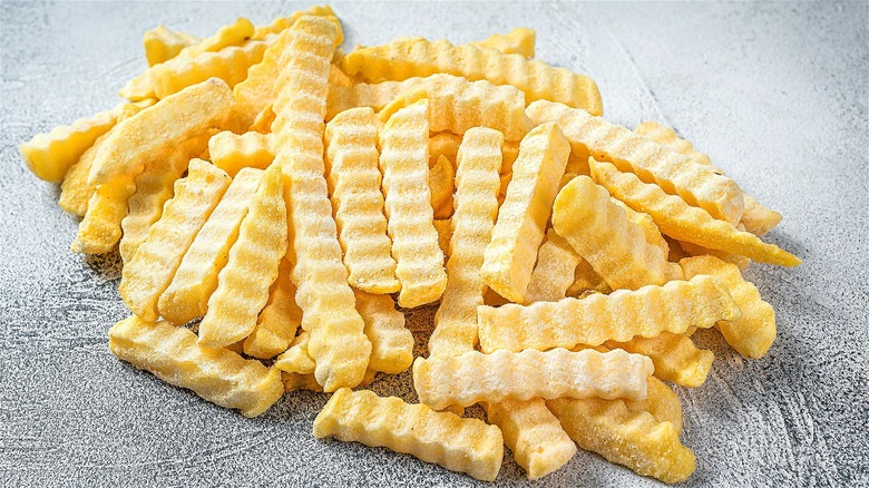 Pile of frozen crinkle-cut fries on a gray surface