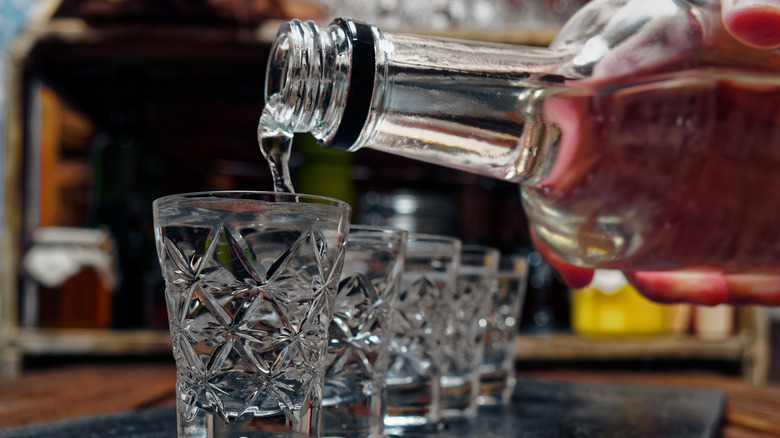 Pouring bottle of vodka into shot glasses