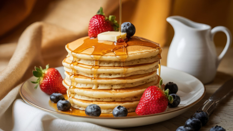 Stack on pancakes topped with butter, strawberries, blueberries, and maple syrup.