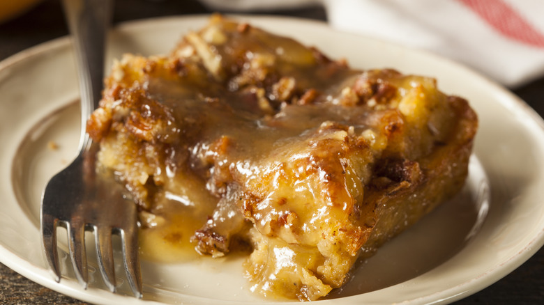 A piece of bread pudding drizzled with sauce on a plate with a fork
