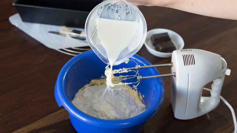 adding milk to cake batter with hand mixer