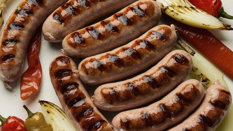 A plate full of grilled sausages has grilled peppers and onions