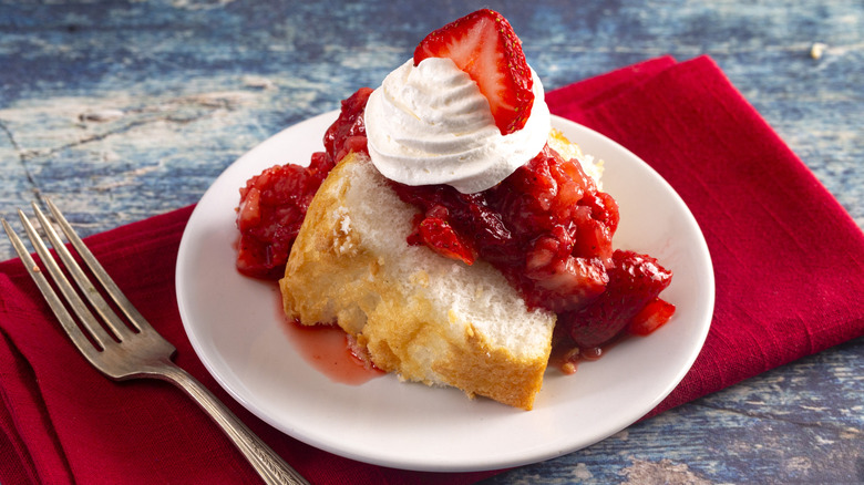 A slice of angel food cake topped with strawberries and whipped cream on a red napkin