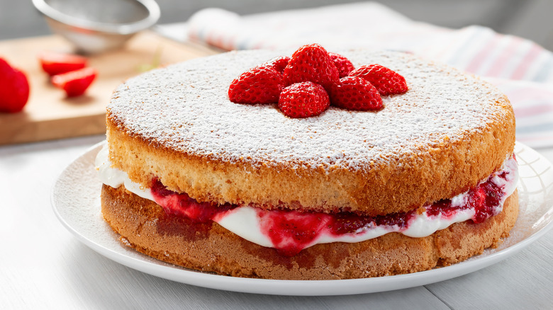 A two-layer sponge cake with creak and berries topped with powdered sugar and berries