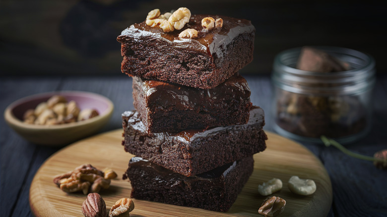 A stack of cleanly sliced fudgy chocolate brownies topped with nuts on a wooden board