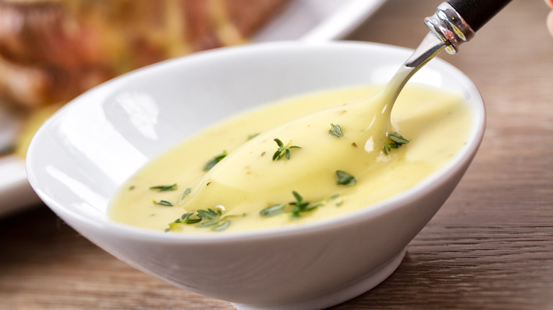 A creamy sauce with fresh herbs in a white dish with a spoon