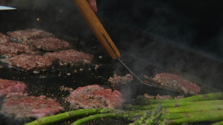 Smash burgers cooking on an outdoor flat top griddle.