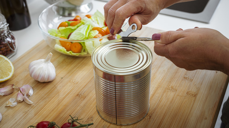 A pair of hands uses an old-fashioned can opener.