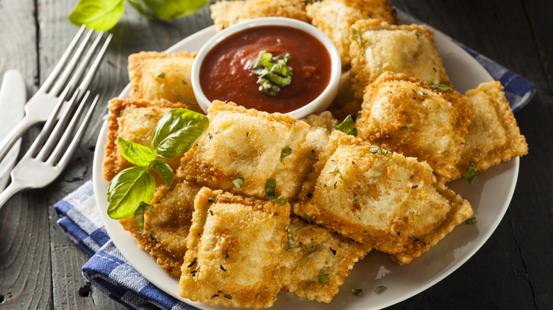 a plate of crispy ravioli with basil and marinara dipping sauce.