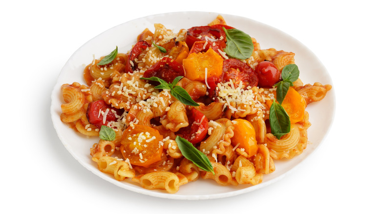 a white bowl of pasta with a burst cherry tomato sauce, cheese, and basil.