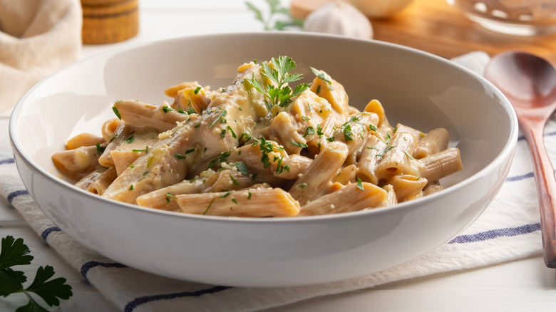 a bowl of penne pasta with alfredo sauce, chicken, and herbs.