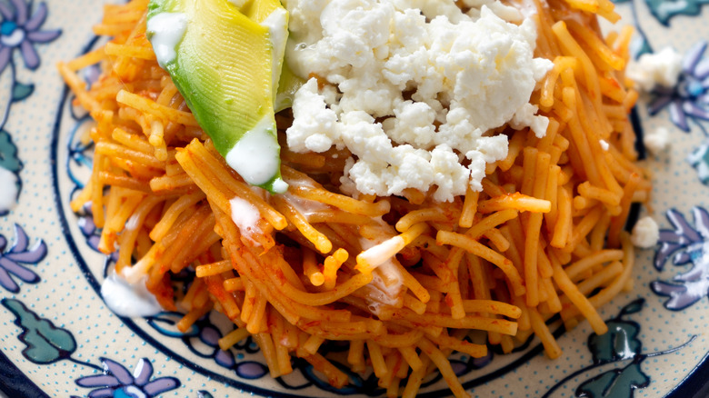 a plate of fideo, a Mexican noodle dish, with crumbled white cheese and avocado.