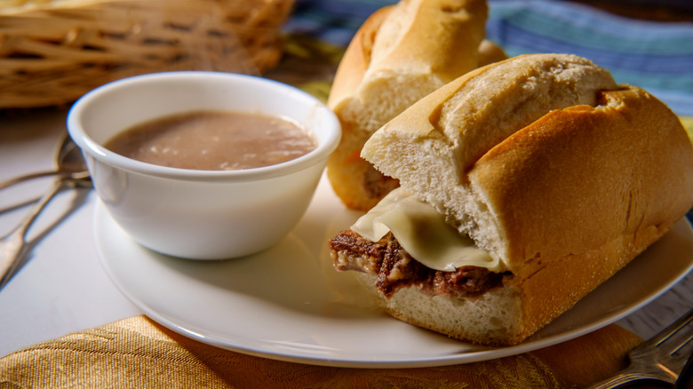 A French dip sandwich sits next a dish of au jus.