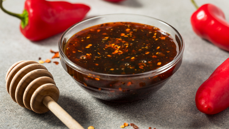A homemade bowl of hot honey with chile flakes is surrounded by fresh chiles.