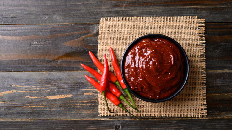 A bowl of gochujang next to hot peppers