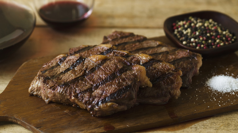 Grilled Delmonico steaks on a board with salt and pepper.