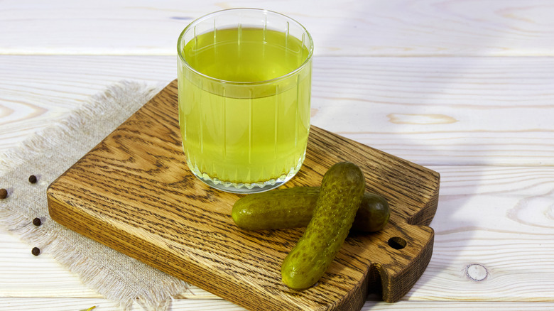 Glass of pickle juice with pickles on wooden serving tray