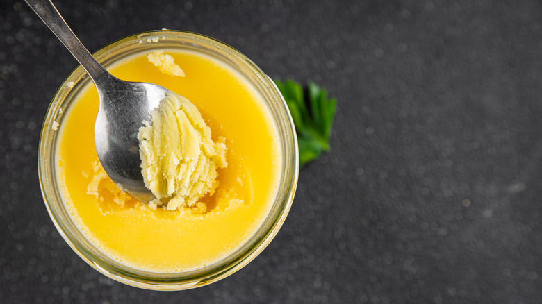 Spooning ghee out of a jar over a black countertop