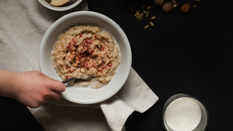 A child's hand stirs a bowl of oatmeal with a spoon