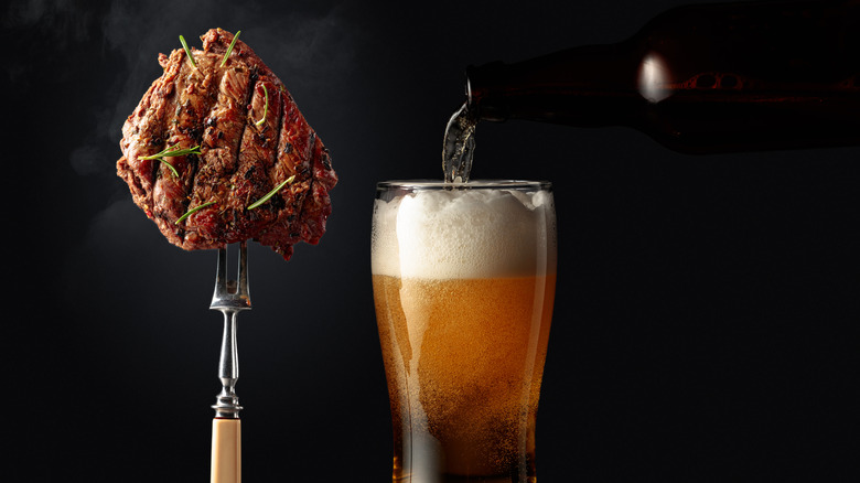 A dark beer sits beside a meat fork with a grilled steak on its tines