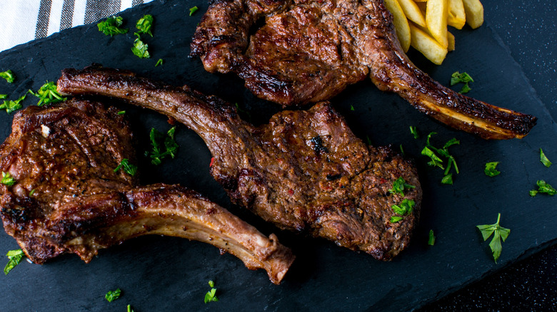 Closeup of grilled lamb shanks with fries on a slate serving board