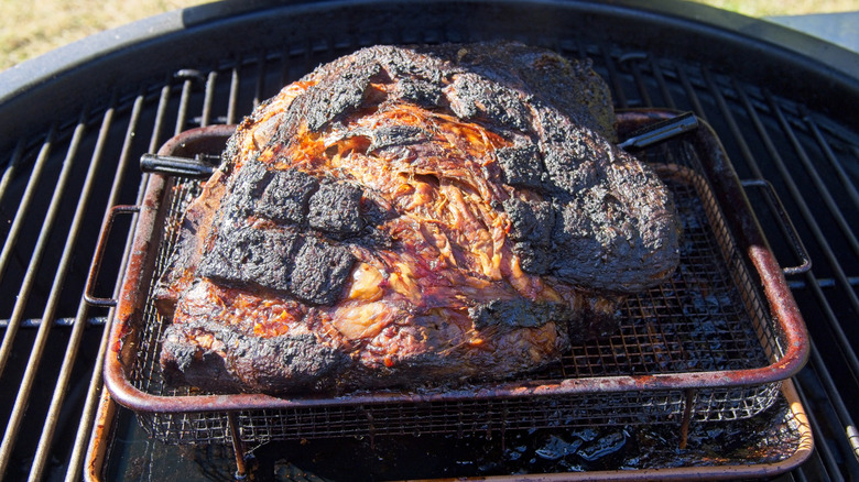A large pork butt is smoked in a basket on a charcoal grill