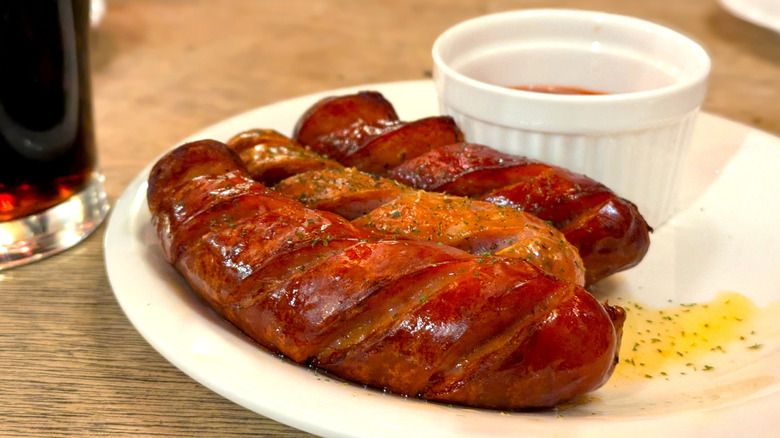 Closeup of grilled sausages on a white plate next to a glass of dark beer