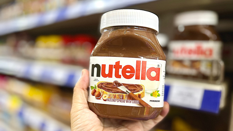 A hand holds up a jar of Nutella in a supermarket