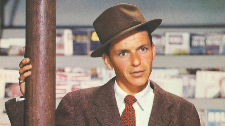 Frank Sinatra stands next to a telephone pole, wearing a hat.