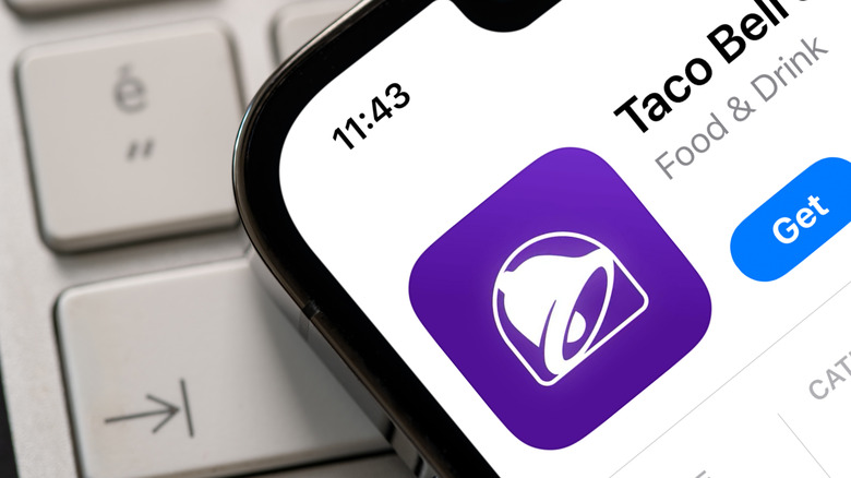 A phone showing the Taco Bell app sits on top of a computer keyboard
