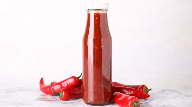 bottle of hot sauce next to chili peppers