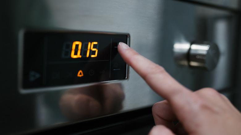 A hand pressing a timer on an oven