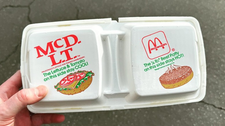 Person's hand holding McDLT burger packaging over concrete