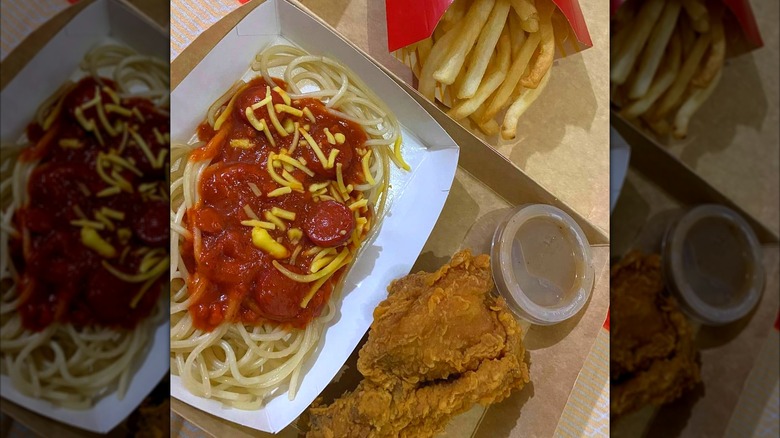 McSpaghetti next to a piece of fried chicken and french fries in a cardboard container