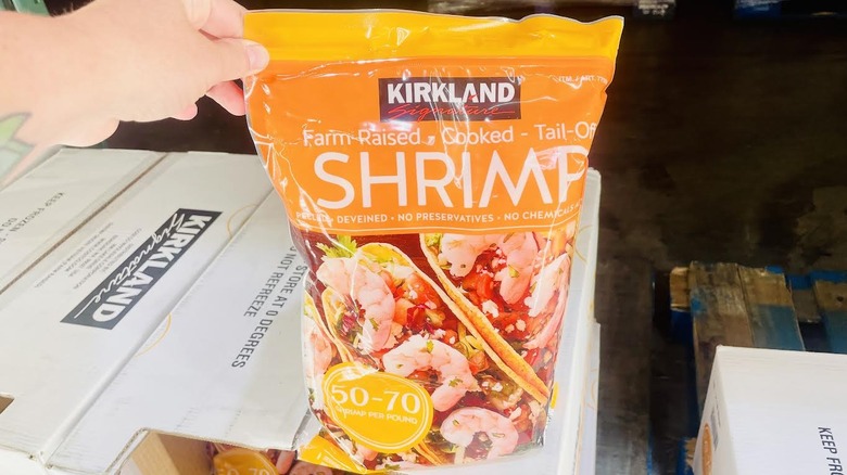Hand holding up bag of frozen Kirkland Signature Cooked Shrimp