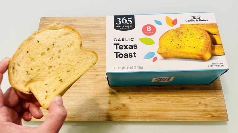 Hand holding slice of 365 by Whole Foods Garlic Texas Toast with box in background