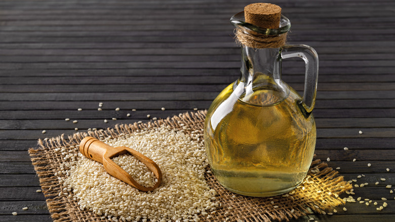 A glass jug of sesame oil alongside sesame seeds