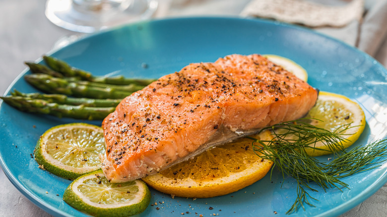 Cooked salmon on a blue plate with slices of lemon and lime as well as spears of asparagus.