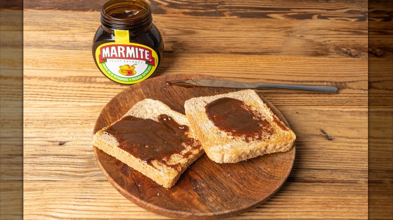 Jar of Marmite next to wood plate with two slices of toast spread with Marmite on wood table